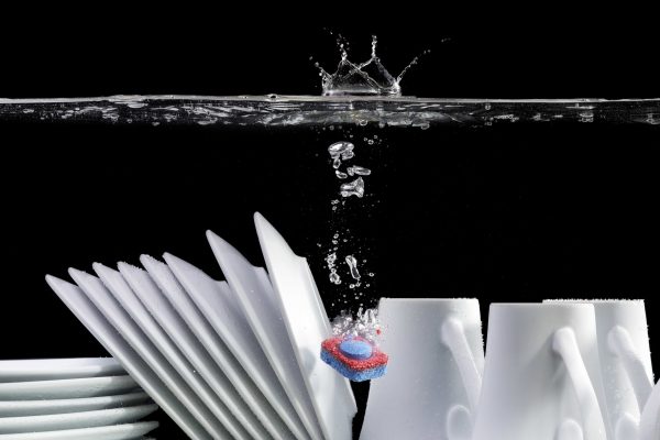 Spültab löst sich über weißem Geschirr auf. Schwarzer Hintergrund.